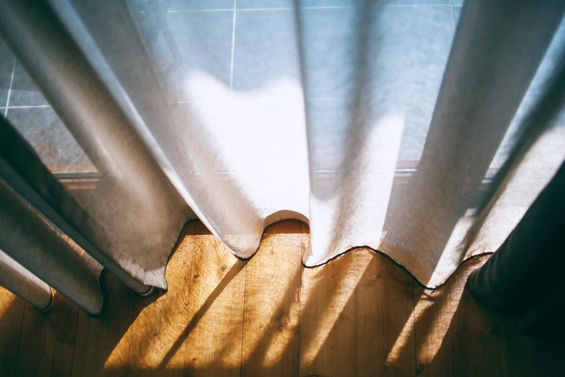 Sunlit curtain hem meeting a wood floor